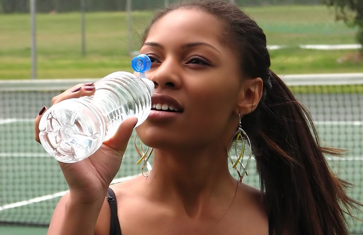 water fast-a-beautiful-teen-african-american-girl-drinking-water-on-a-tennis-court